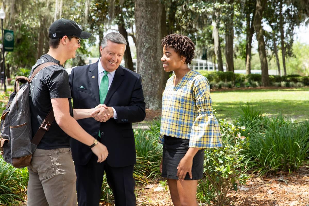 Two students talking with JU President 蒂姆成本 in courtyard on campus